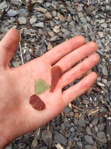 3 pieces of sea glass in my hand: 2 brown, 1 green.